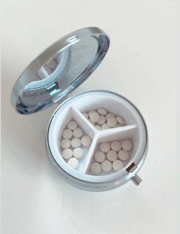 Open pill box showing three small compartments with pills in them 