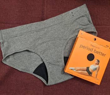 a reviewer photo of a gray pair of the underwear laying out next to the orange packaging 