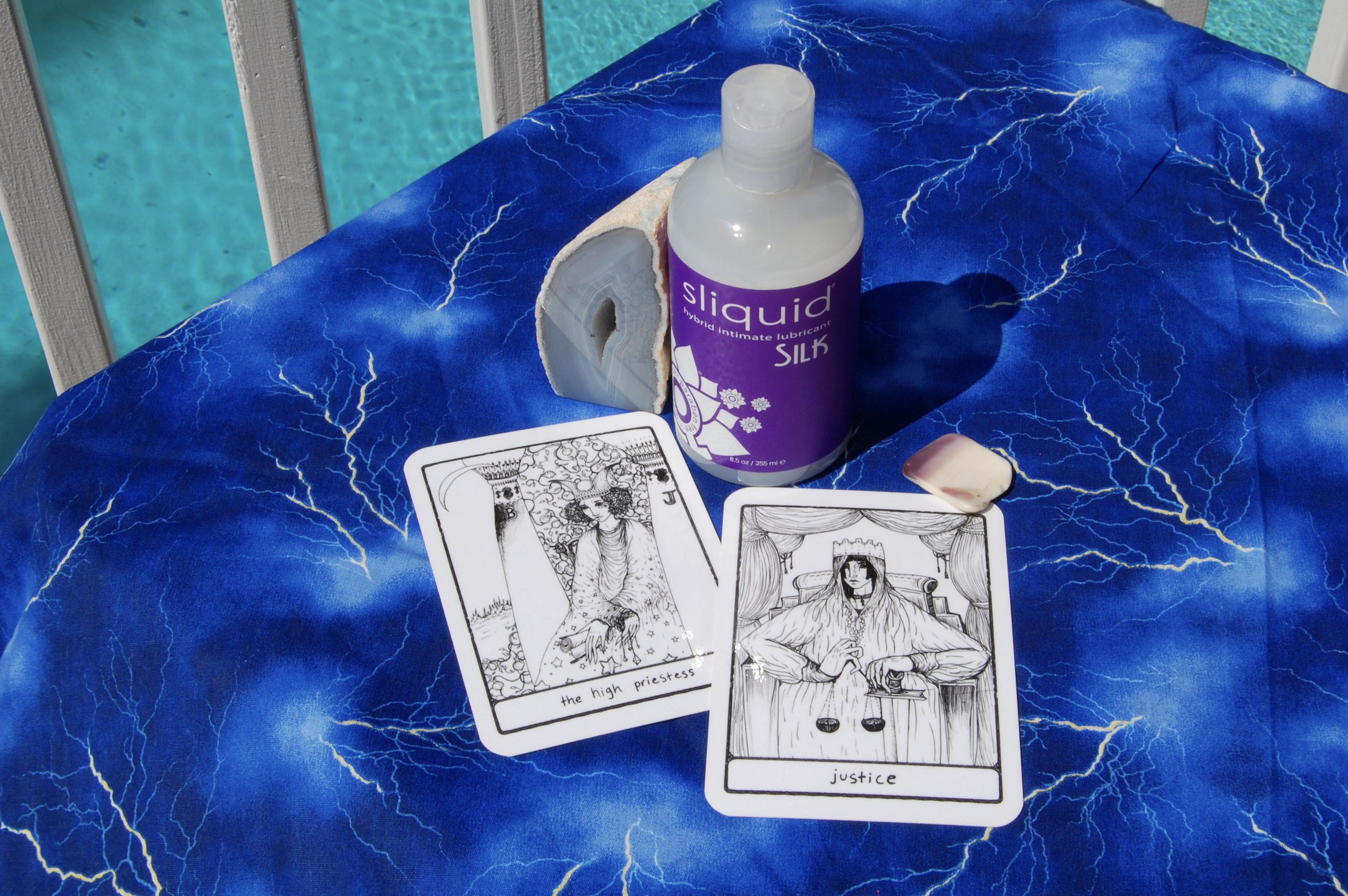 Photo of Sliquid Silk with two tarot cards (The High Priestess and Justice) plus a geode and small, square-shaped shell