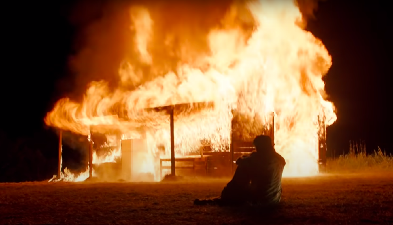 Han Ye-ri and Steven Yeun sitting as they watch their shed burn in "Minari"