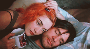 Kate with orange hair, in bed with a man and holding a mug