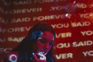 Girl resting her chin on her hand with the words "You Said Forever" on the walls.
