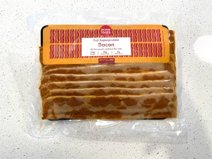 A package of the plant-based bacon in long strips, shrink wrapped in plastic on a cardboard tray