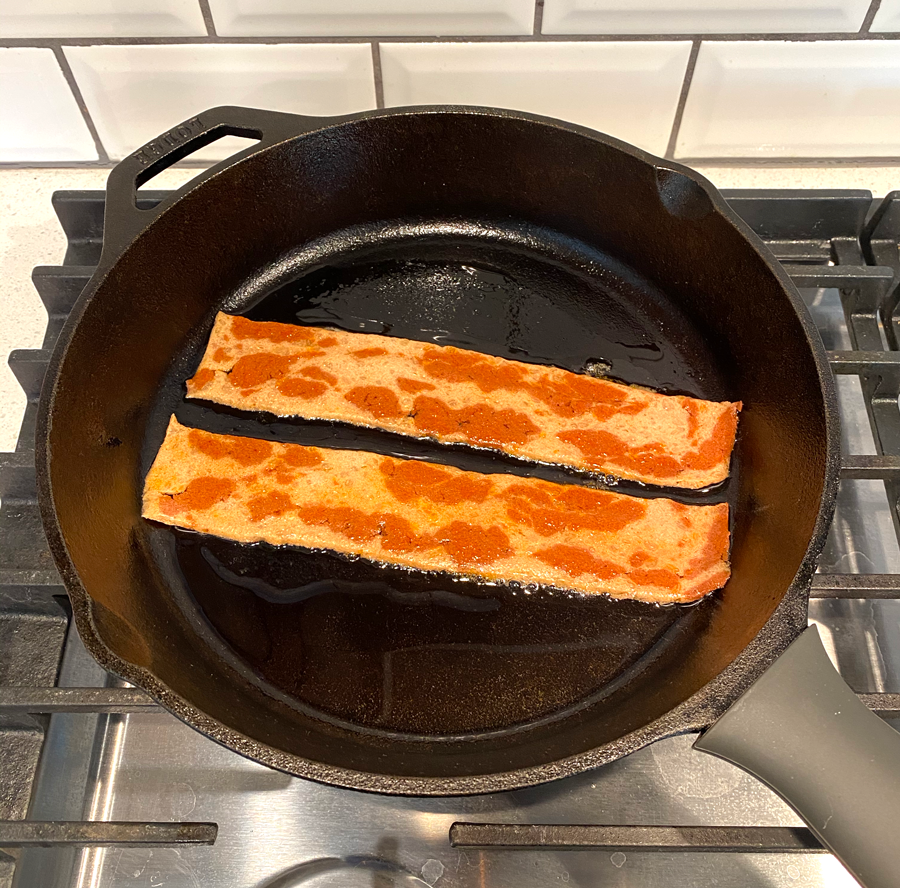 A skillet with two strips of the bacon in it