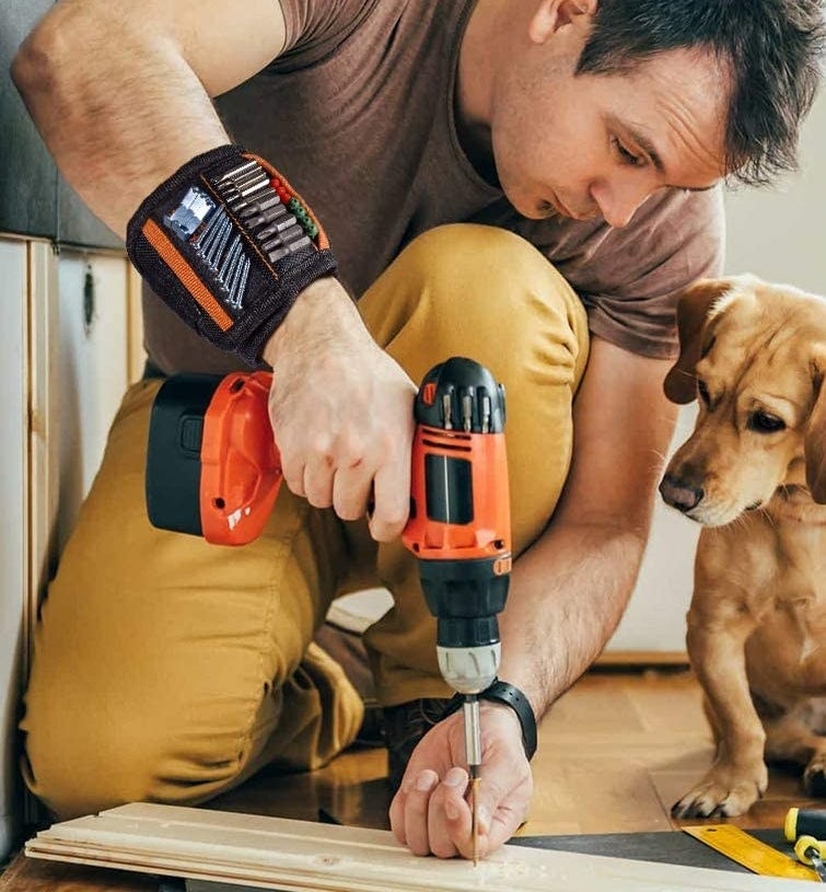 model wearing the band with screws and bits sticking to it as he holds a drill