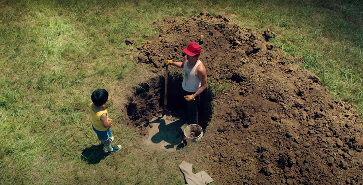 Steven Yeun digging and well and talking to his son, Alan S Kim, in "Minari"