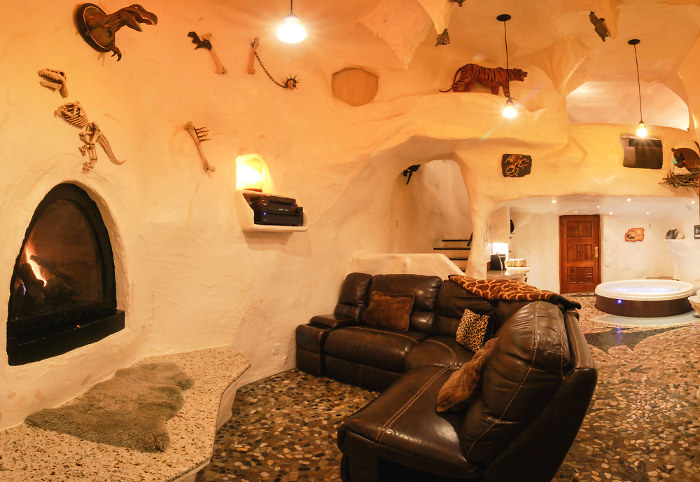 A hotel room that looks underground, with rough white walls, a pebbled floor, a fireplace, and fossils as decorations