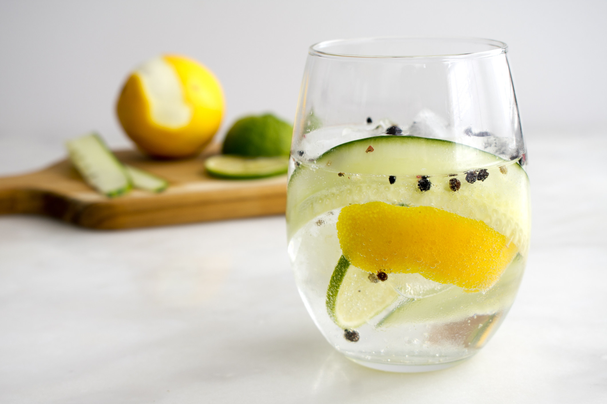 Gin and Tonic with whole black pepper, lemon rind, and cucumber.