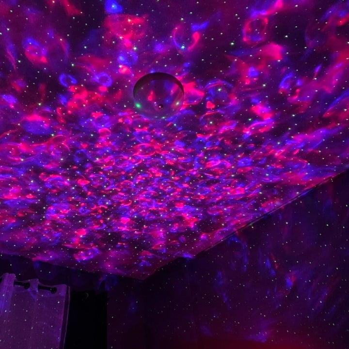 reviewer image of the same bedroom whose walls and ceiling are covered in pink and purple LED ocean wave lights