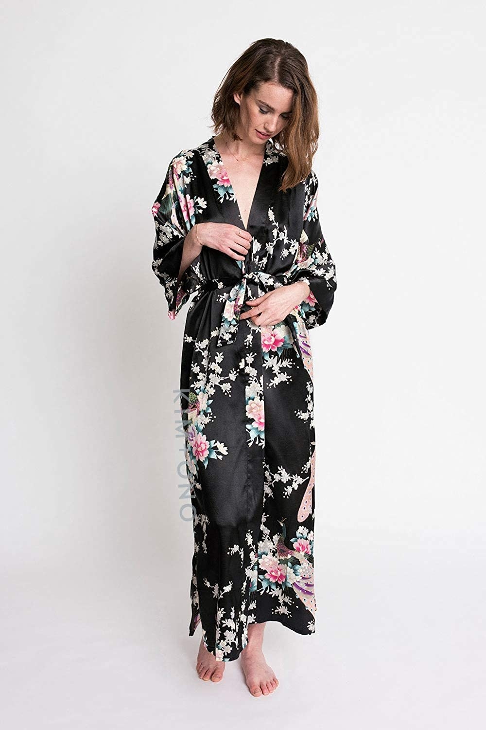 A model wears the KIM+ONO satin kimono robe in the black peacock and blossoms design
