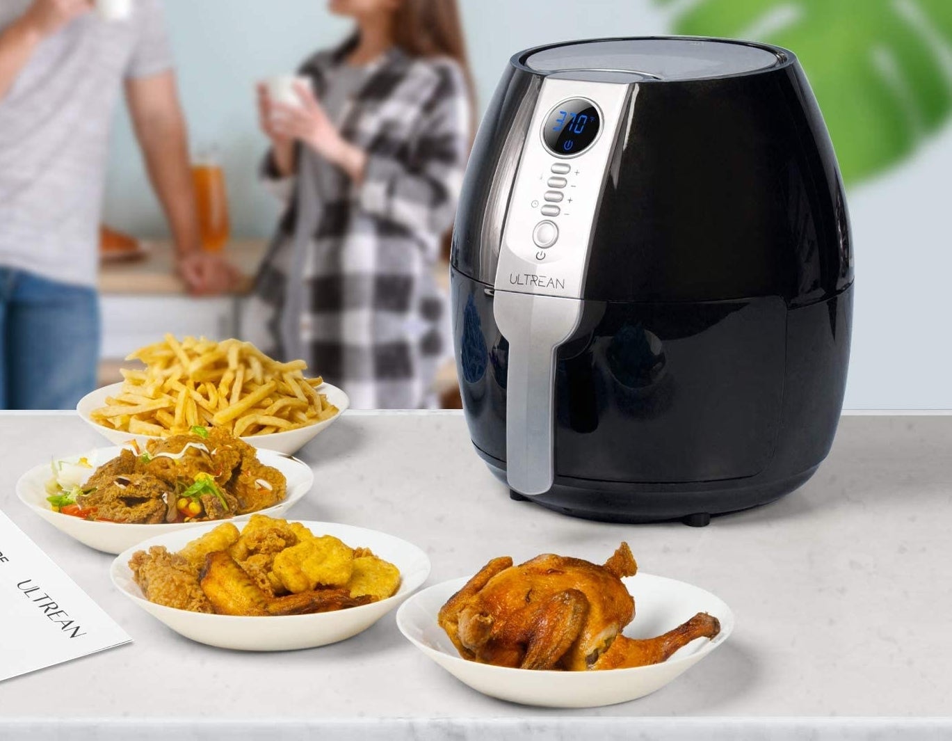 The air fryer on a table surrounded by chicken and fries