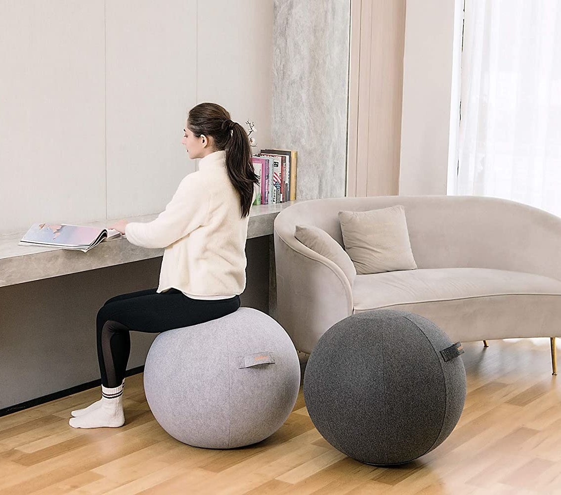 A person sitting on a ball next to a second ball in a living room 