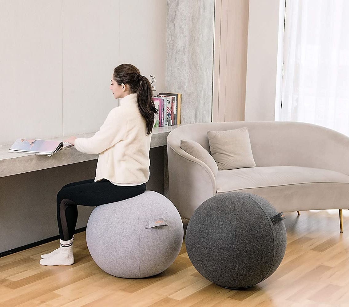 A person sitting on a ball next to a second ball in a living room