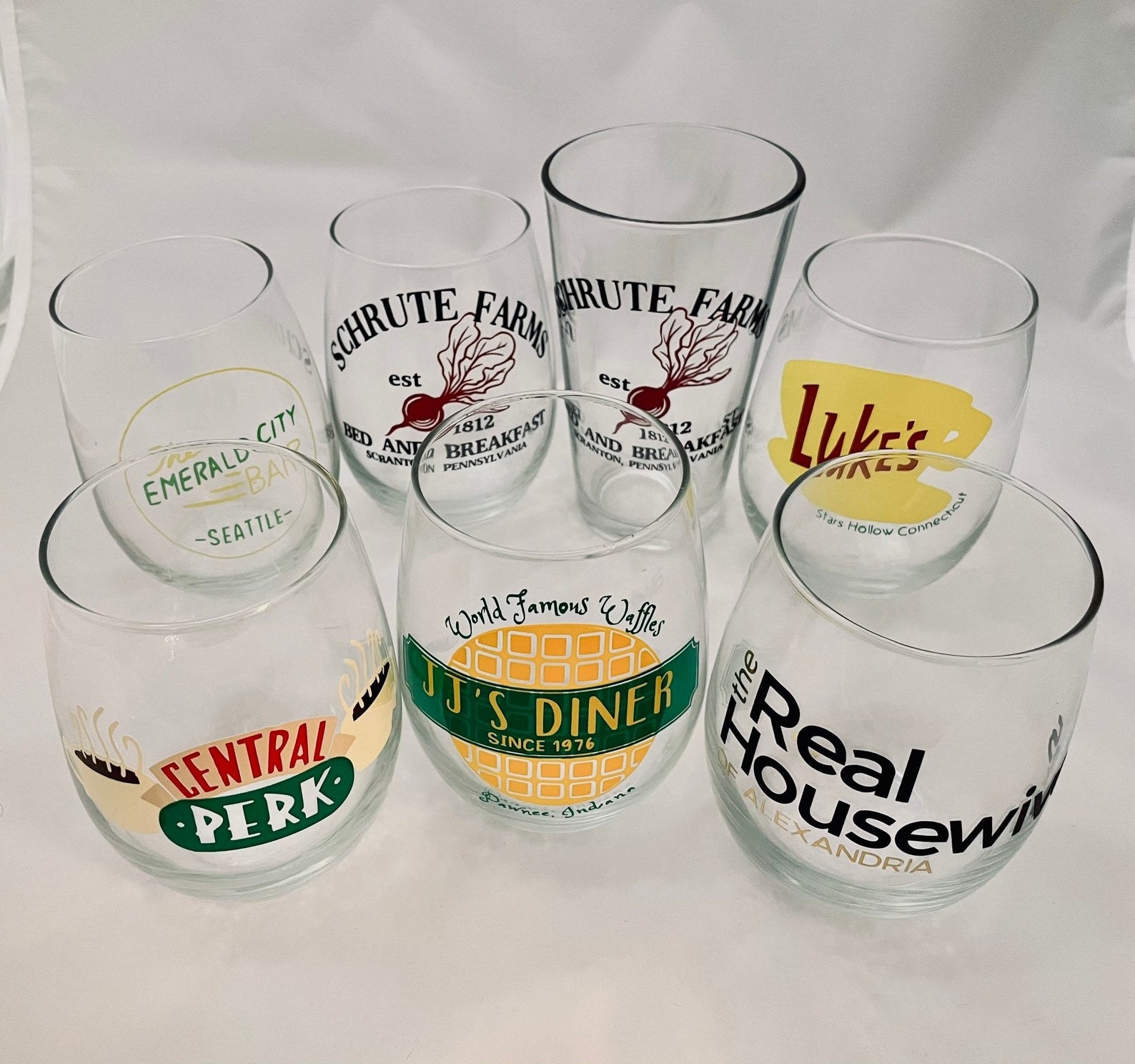 Wine glasses with logos for Central Perk, Real Housewives, JJ&#x27;s Diner, Luke&#x27;s Coffee Shop, Schrute Farms, and Emerald City Bar 