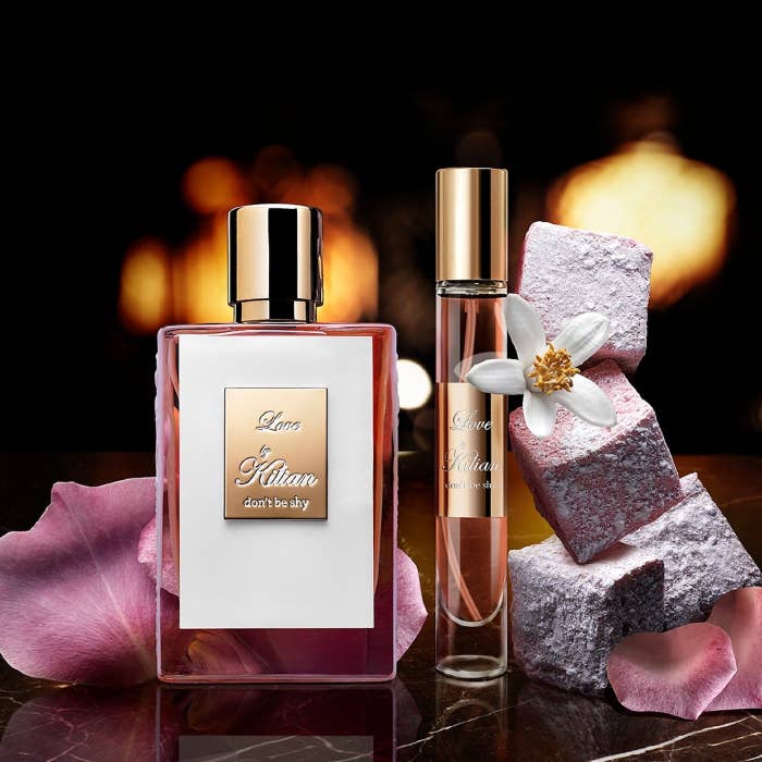 Two bottles of perfume on table next to pink stones and flowers