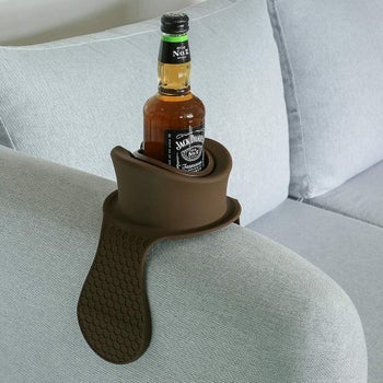 The brown plastic cup holder attached to the arms of a couch with a beer bottle in it 