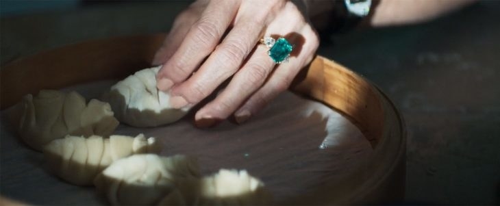 Closeup of hand with giant emerald ring placing a freshly wrapped dumpling in a steamer 