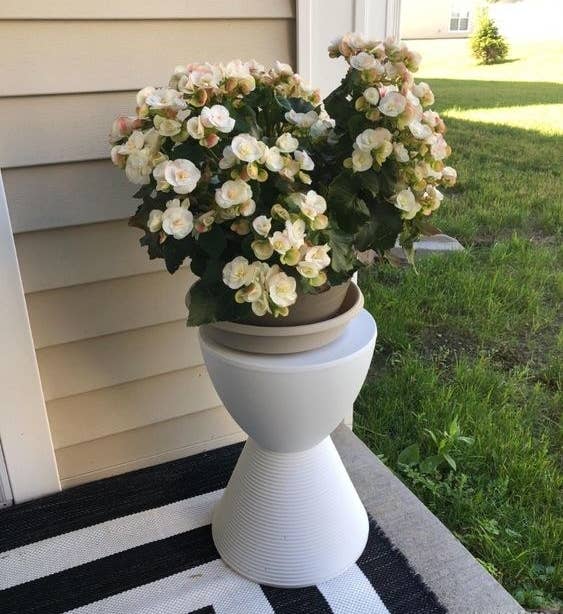 Reviewer using the hourglass-shaped accent stool in white to hold flowers at their doorstep 