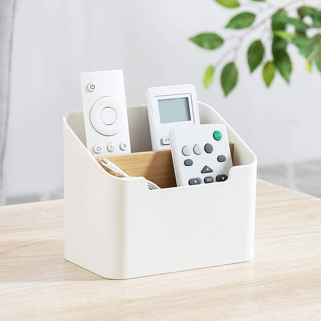 A white and light wood rectangle-shaped holder with two compartments for remotes to rest in upright 