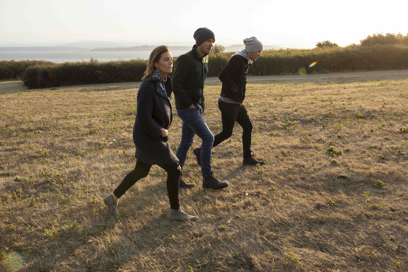 Brandi walks with two men in a field, all dressed in jeans and warm coats