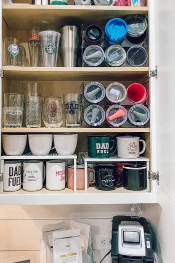 a reviewer photo of water bottles inside the water bottle storage organizer inside of a pantry with room for other glasses and coffee mugs