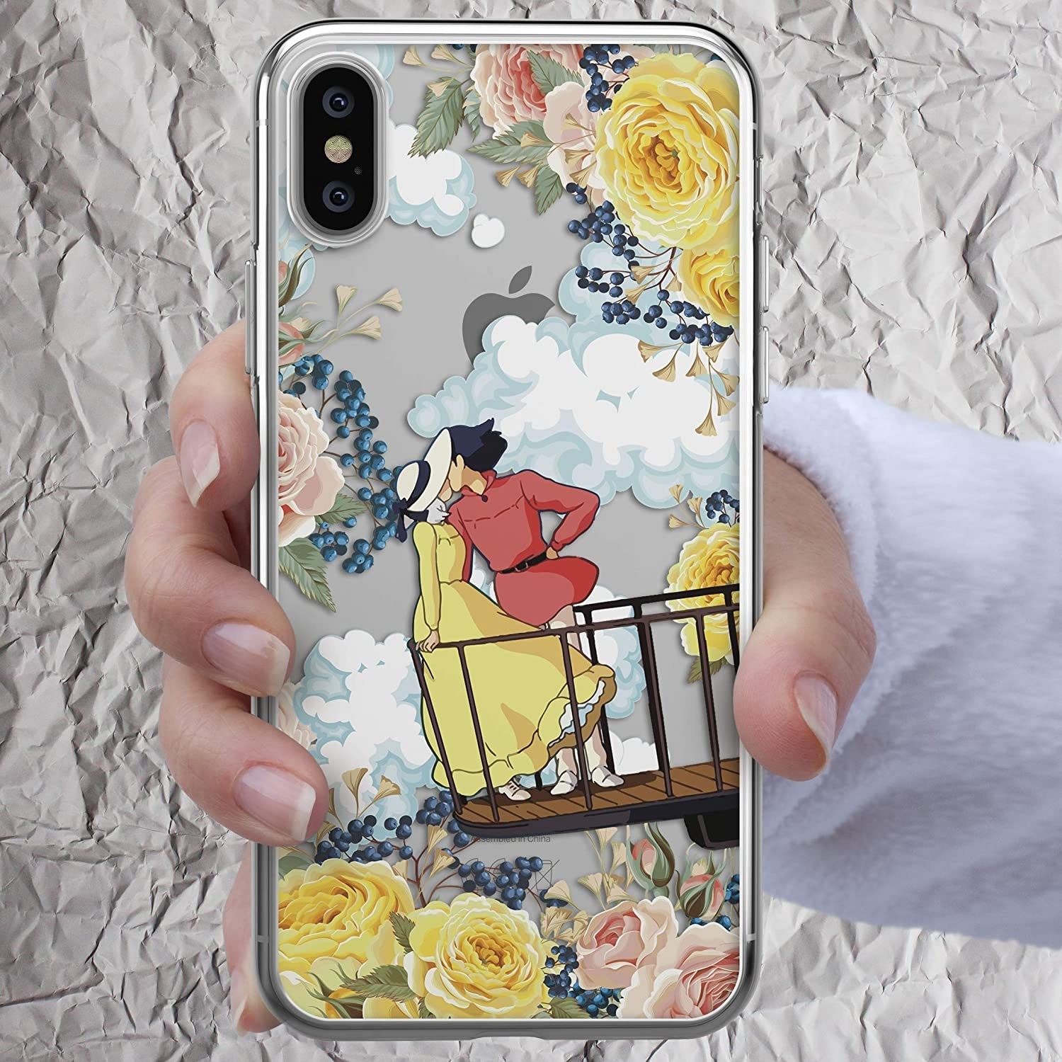 hand holding a phone with the clear case printed with yellow and pink flowers, clouds, and the shot of Howl and Sophie kissing on the balcony from the end of the movie