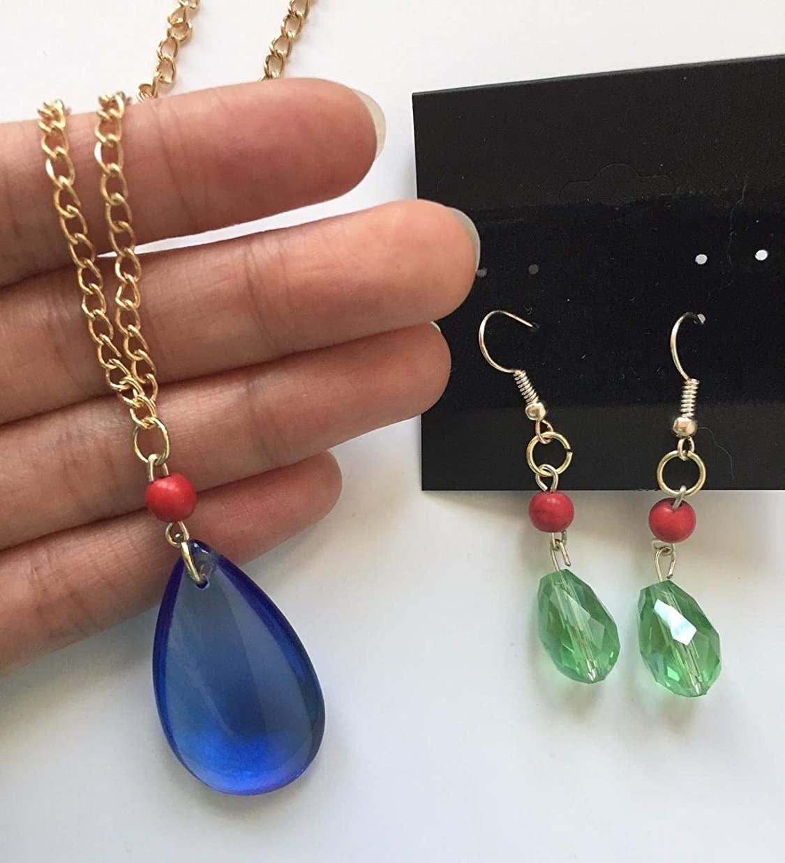 hand holding the blue teardrop necklace next to the green drop earrings