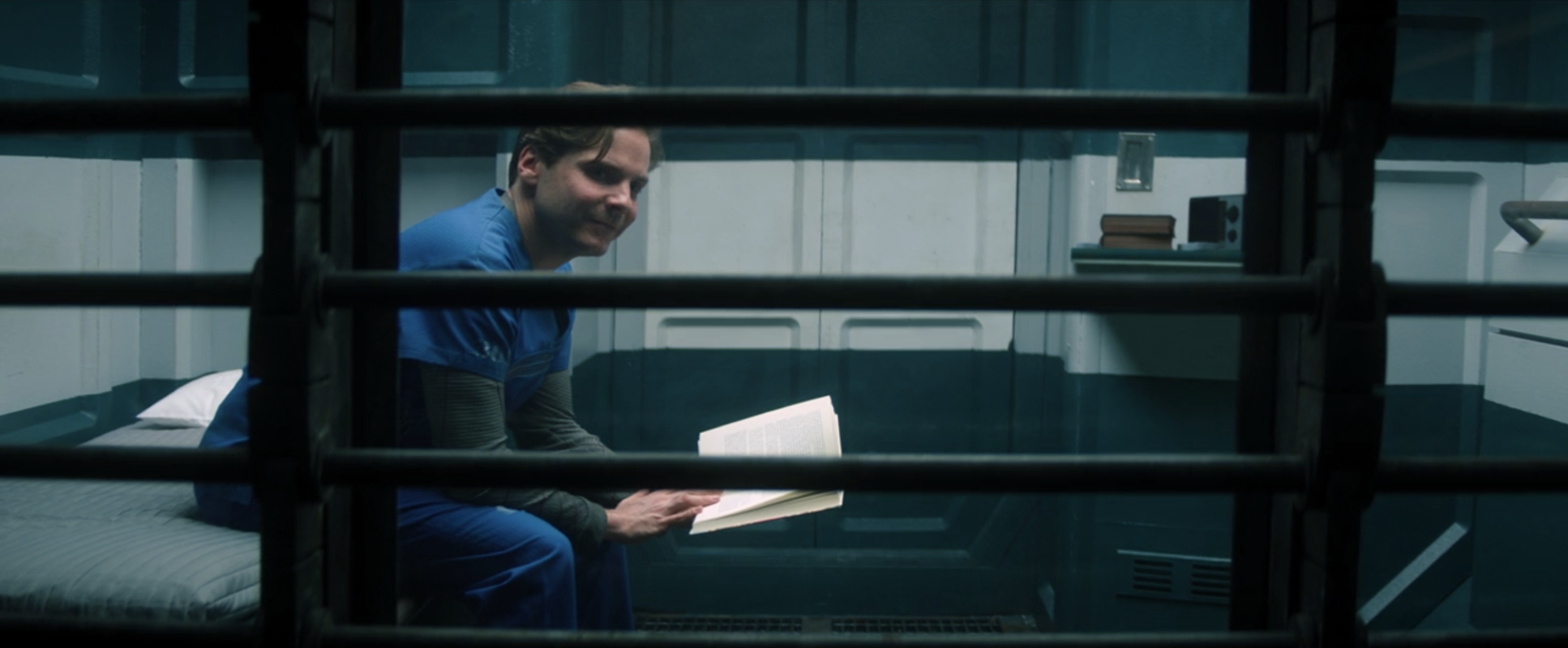 Zemo sitting on his bed in his prison cell reading a book and smiling