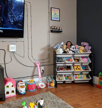 the toy organizer filled with toys in the corner of a room to show the amount of space it will take up in a room