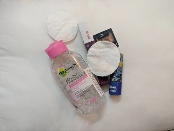 The bottle of micellar water pictured with a few lipsticks and cotton pads.