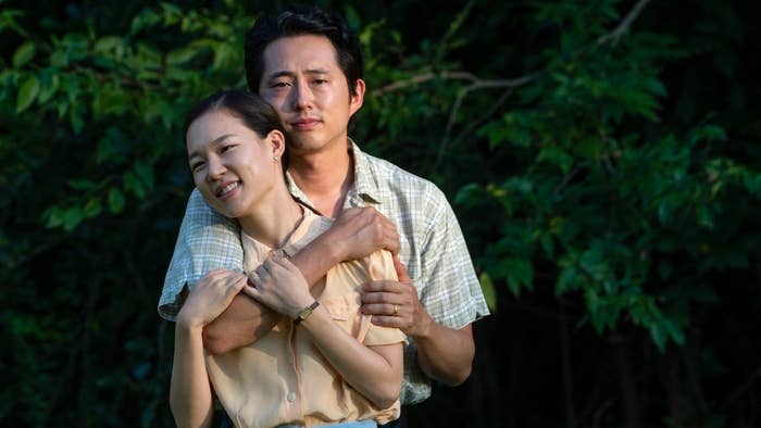 Jacob standing behind Monica (from "Minari") with his arm around her. They are standing in front of a dark green bush.
