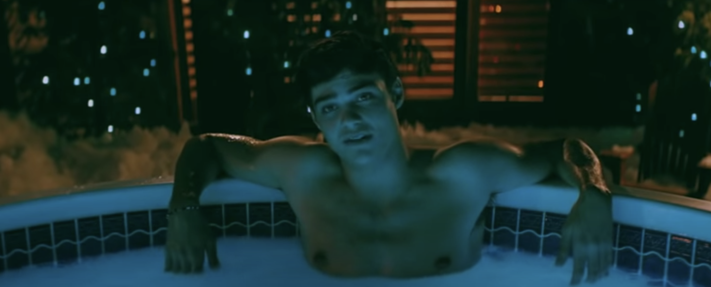 A teen boy is sitting in a hot tub with his arms leaning against the edge as he faces a character who's not revealed
