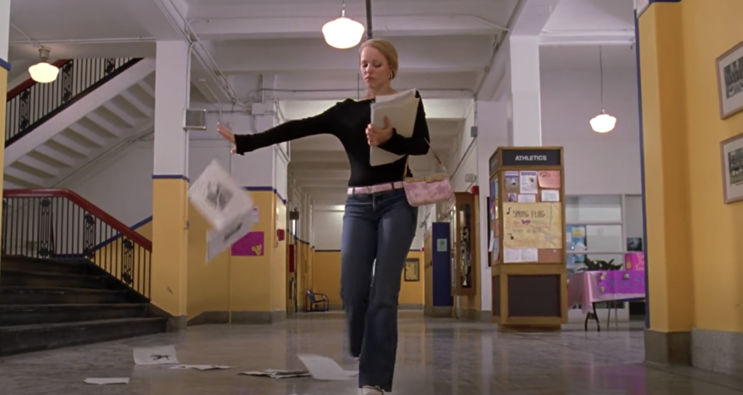 Regina George is walking down a hallway, throwing papers in the air