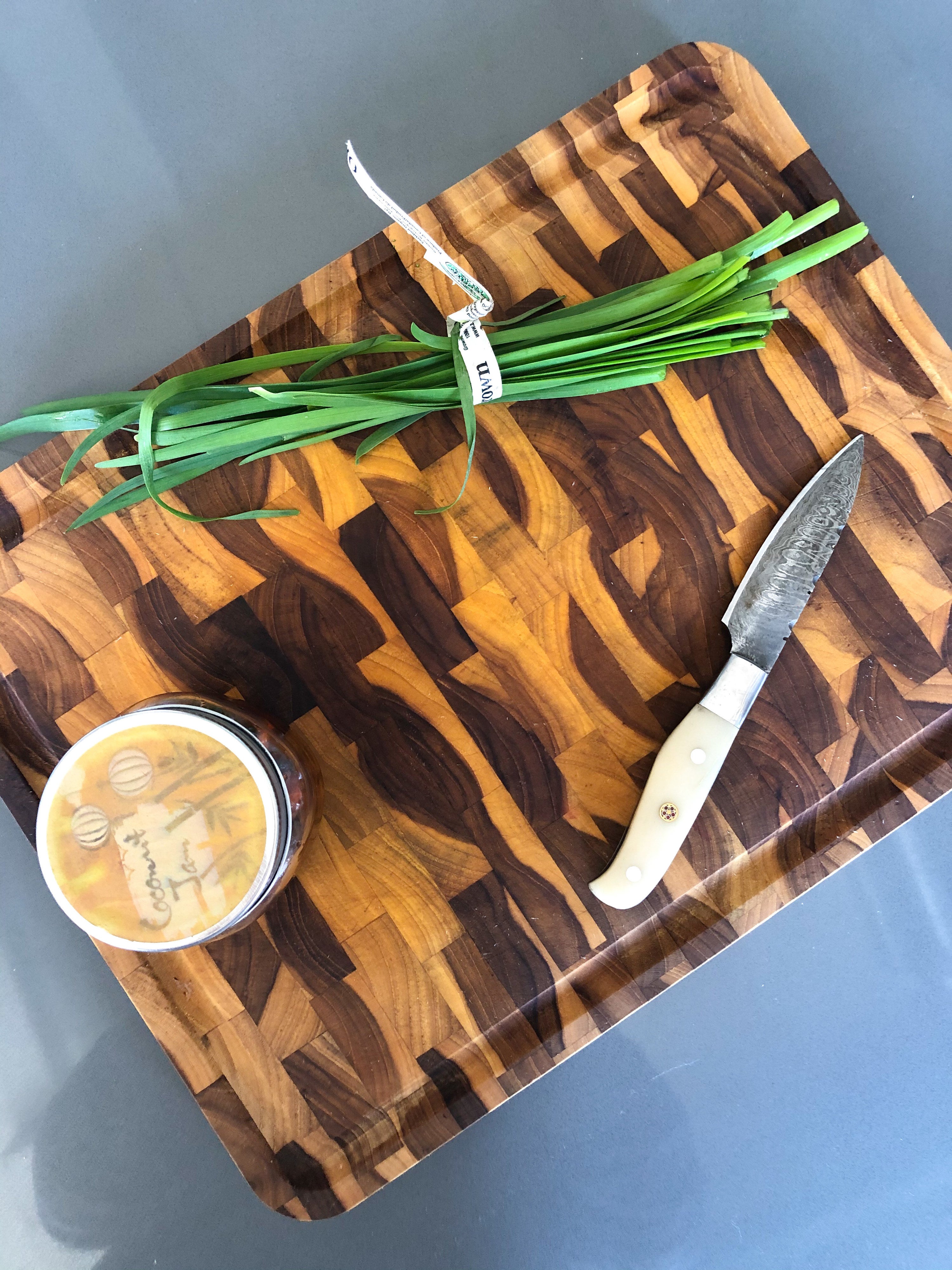 A flatlay of the end-grain butcher block cutting board with a chic knife and fresh herbs on top