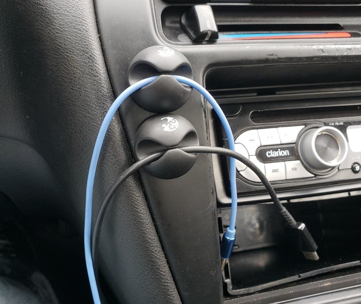 a reviewer photo of the cable clips mounted onto a car dashboard with charging cables secure in them 