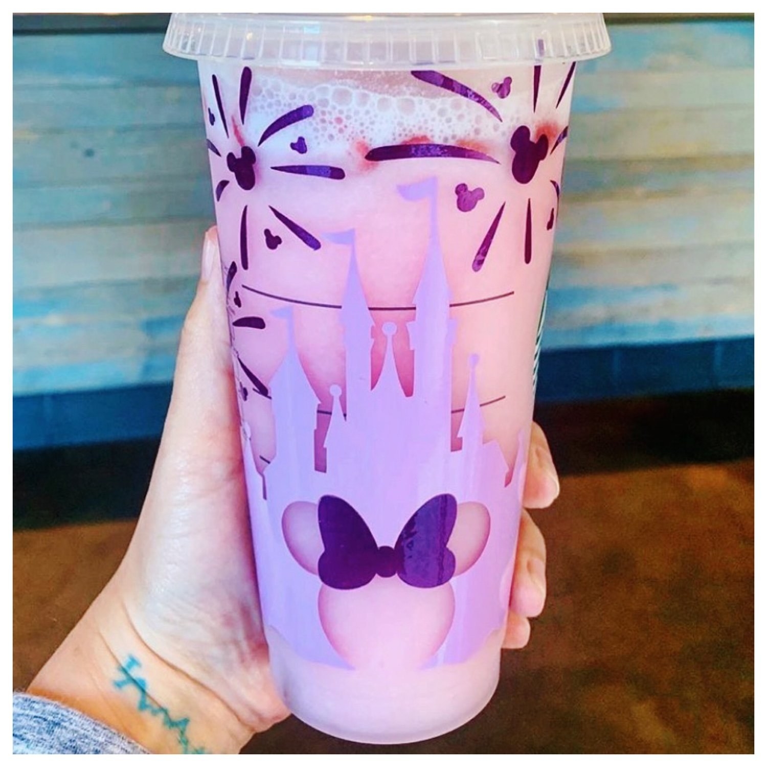 A model holding a clear Starbucks cold cup with a purple Disney castle and Minnie Mouse design on it 