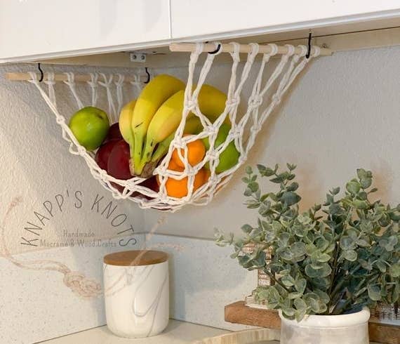 a macrame hammock hanging from underneath a kitchen cabinet with fruits in it 