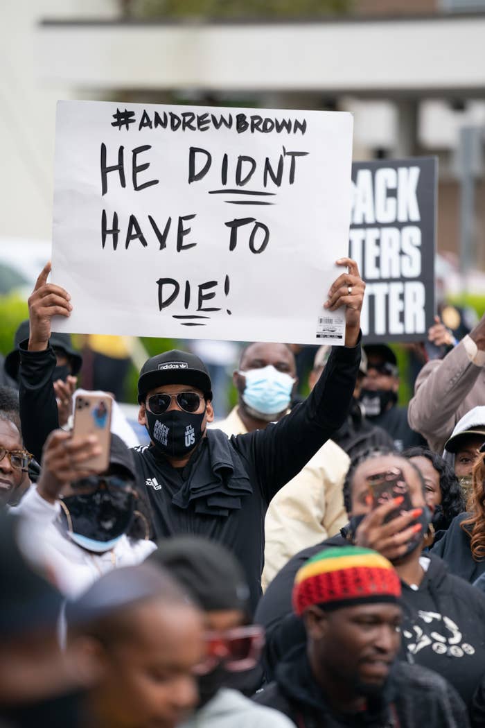 A man holds up a protest sign in a crowd reading &quot;Hashtag Andrew Brown / He didn&#x27;t have to die&quot;