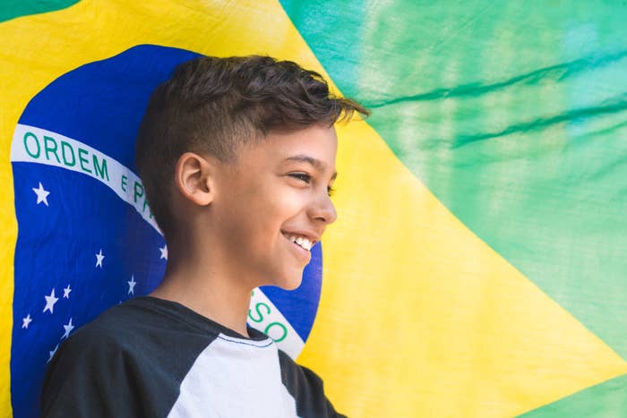 A boy smiles in front of the Brazilian flag