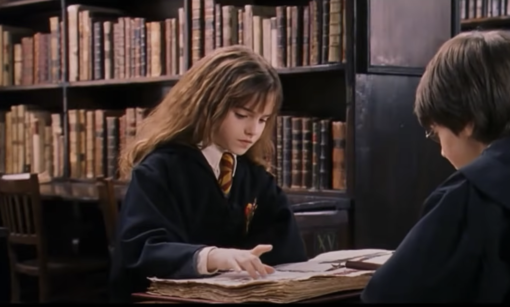 Hermoine Granger and Harry Potter look through a book at the library to find a spell
