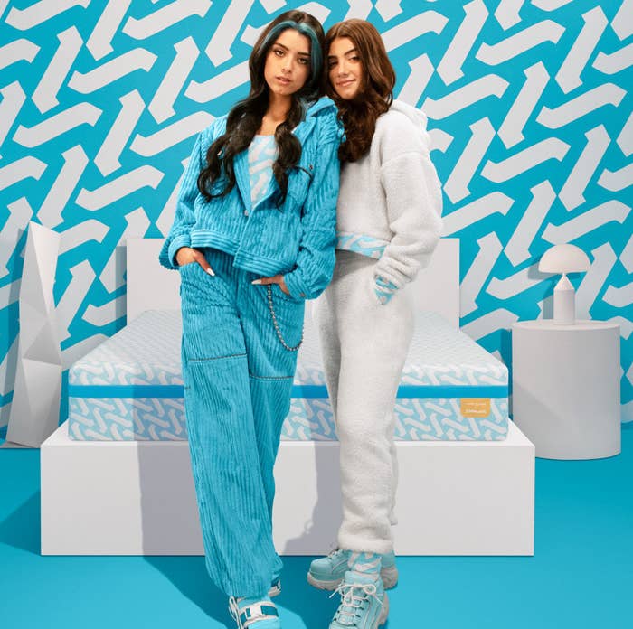 Charli and Dixie D&#x27;Amelio stand in front of their mattress in a vivid blue and white room.