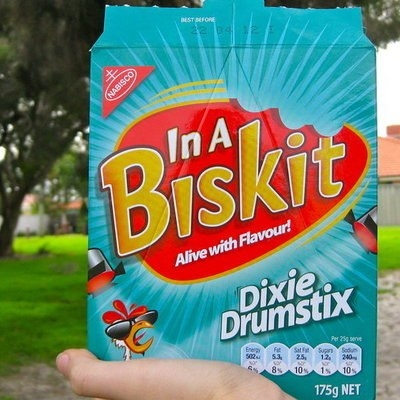 A box of In A Biskit Dixie Drumstix flavour being held up by a hand 