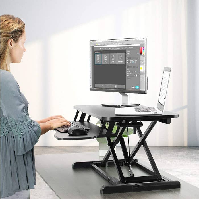 A person standing to use their computer which is placed on top of the standing desk attachment 