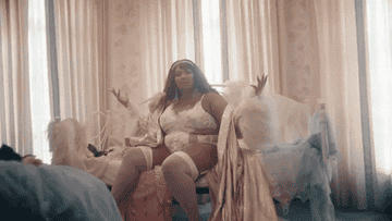 Lizzo is sitting on a couch while lifting her hands