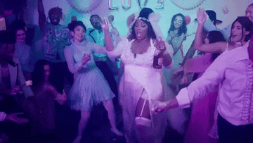 Lizzo is wearing a wedding gown while holding a bottle in her hand