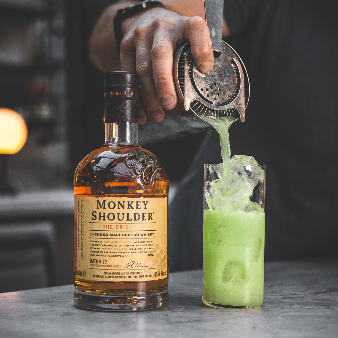 green cocktail being strained into a glass next to a bottle of monkey shoulder whisky