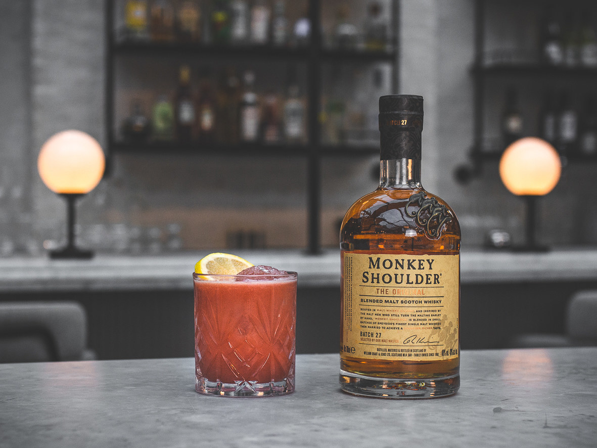 red cocktail  in tumbler next to a bottle of monkey shoulder whisky