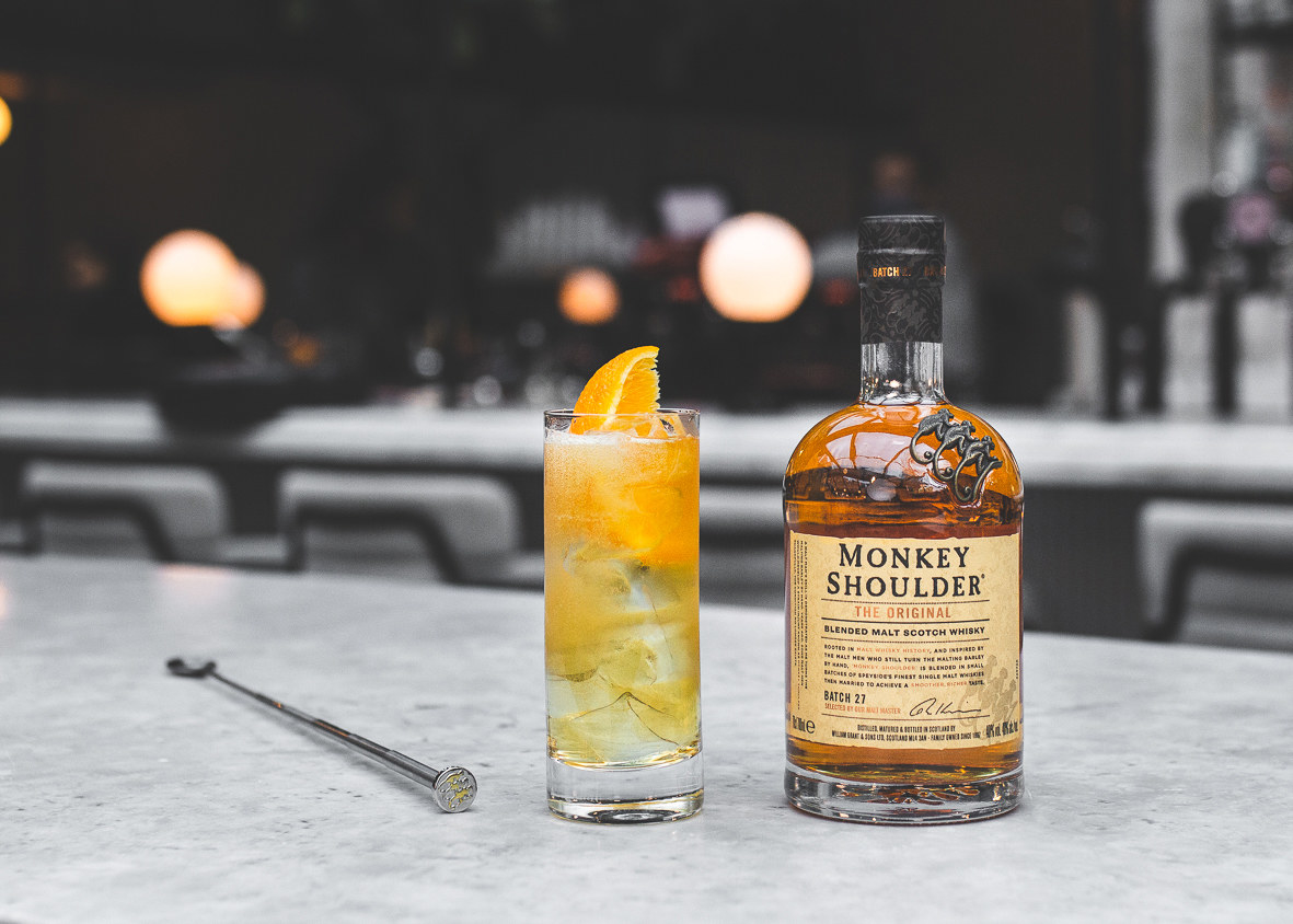 orange cocktail  in glass next to a bottle of monkey shoulder whisky