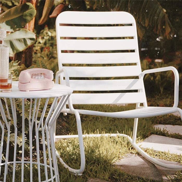 Low white piping rocking chair in grassy backyard 