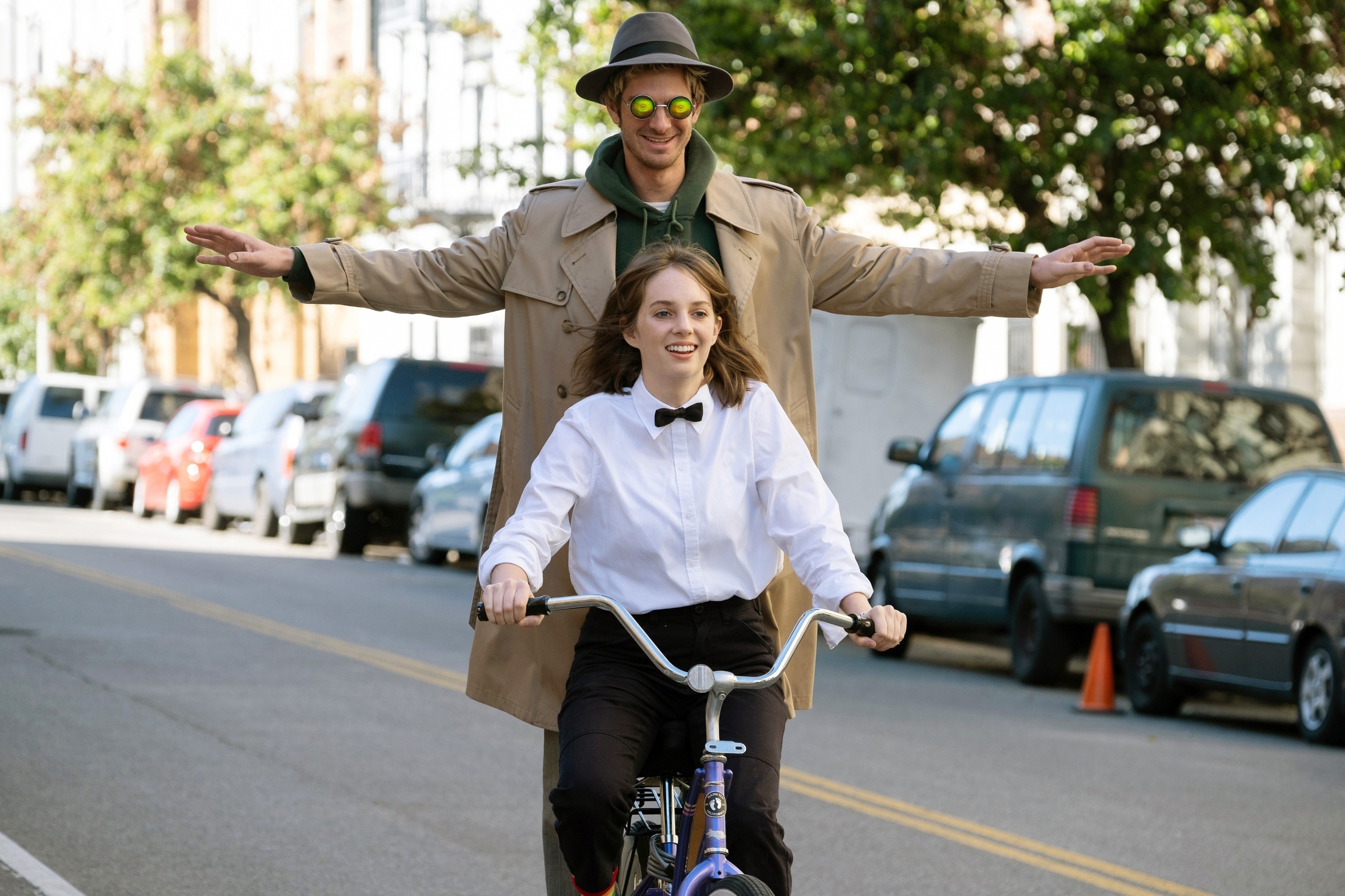 Andrew Garfield and Maya Hawke riding on a bicycle in the street 